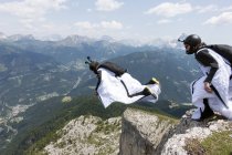 Dos saltadores BASE macho que salen de la cima de la montaña, Dolomitas, Italia - foto de stock