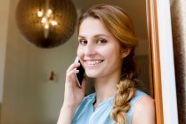 Retrato de mujer joven charlando en el teléfono inteligente en la puerta de la cafetería - foto de stock