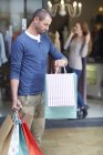 Mujer joven de compras, hombre fuera sosteniendo bolsas, mirando el reloj - foto de stock