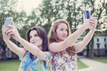 Дві молоді друзі-жінки беруть селфі на смартфонах поруч — стокове фото