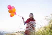 Jovem mulher no monte gramado segurando monte de balões — Fotografia de Stock
