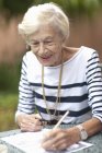 Senior woman drawing in retirement villa garden — Stock Photo