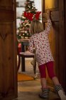 Menina verificando na árvore de Natal atrás da porta em casa — Fotografia de Stock