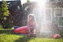 Chica joven jugando en aspersor de jardín - foto de stock