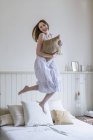 Mulher vestindo vestido branco pulando na cama olhando para a câmera sorrindo — Fotografia de Stock