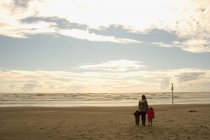 Mother with son and daughter holding hands on sandy beach — Stock Photo