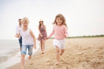 Família correndo ao longo da praia arenosa — Fotografia de Stock