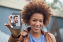 Young woman holding up smartphone with photograph of boyfriend — Stock Photo