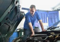 Мужской механик проверяет двигатель автомобиля в гараже — стоковое фото