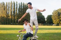 Two male friends fooling around on bicycle in park — Stock Photo