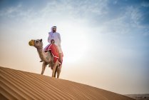 Mann in traditioneller mittelöstlicher Kleidung reitet Kamel in Wüste, Dubai, vereinigte arabische Emirate — Stockfoto