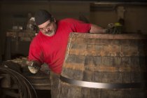 Male cooper using hammer in cooperage with whisky casks — Stock Photo