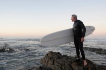Surfista em pé na praia rochosa — Fotografia de Stock