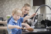 Mother helping son wash wooden spoon — Stock Photo