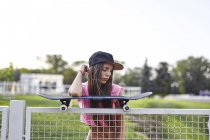 Молода жінка балансує скейтборд на металевому паркані, лікоть на скейтборді — стокове фото