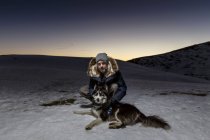 Портрет взрослого человека, приседающего с собакой в снегу ночью — стоковое фото