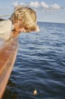 Мальчик, висящий на лодке в голубом океане — стоковое фото