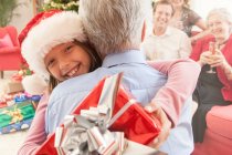 Petite-fille tenant cadeau de Noël embrassant grand-père souriant — Photo de stock