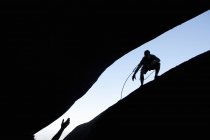 Silhouetten männlicher Kletterer, die sich auf Felsen gegenseitig die Hand reichen — Stockfoto