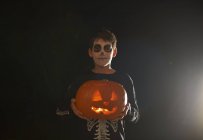 Retrato de menino vestindo halloween esqueleto fantasia segurando abóbora — Fotografia de Stock