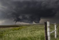 Une grande tornade de cône se pose dans un champ ouvert à partir de grands nuages muraux inclinés — Photo de stock