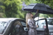 Mujer joven luchando para poner paraguas - foto de stock