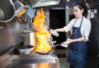Asiático hembra chef flambeing en comercial cocina - foto de stock