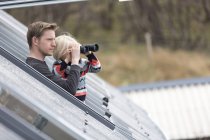 Padre e figlio che guardano attraverso il tetto, ragazzo usando il binocolo — Foto stock