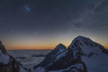 Засніжені гірські вершини та освітлене зоряне небо — стокове фото
