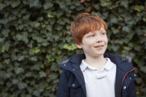 Portrait of red haired boy in front of ivy wall looking away — Stock Photo
