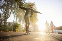Giovane skateboarder skateboard maschile sulla strada illuminata dal sole — Foto stock