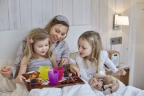 Mother and daughters having breakfast in bed — Stock Photo