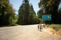 Family standing at roadside by sign saying welcome to California — Stock Photo