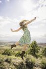 Молодая женщина в платье и ковбойских сапогах, прыгающая в пейзаж, Бриджер, Монтана, США — стоковое фото
