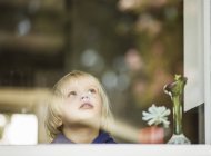 Garçon d'âge préscolaire à la fenêtre de la maison regardant vers le haut — Photo de stock