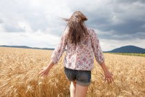 Mid adult woman walking through wheat field — Stock Photo