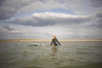 Seniorin sitzt auf Surfbrett im Meer — Stockfoto