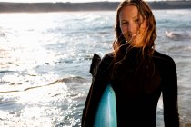 Женщина, стоящая с доской для серфинга и улыбающаяся — стоковое фото