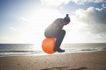 Mature man jumping mid air on inflatable hopper at beach — Stock Photo