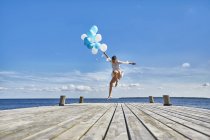 Junge Frau tanzt auf Holzsteg und hält ein Bündel Luftballons in der Hand — Stockfoto
