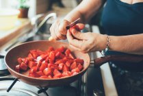 Cropped image of mature woman chopping tomatoes into saucepan — Stock Photo