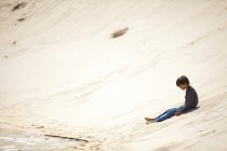 Молодий хлопчик сидить на піщаному пагорбі — стокове фото