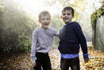 Retrato de meninos gêmeos, ao ar livre, cercado por folhas de outono, rindo — Fotografia de Stock