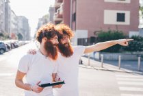 Молоді чоловіки хіпстер близнюки з рудим волоссям і бородою вказують на міську вулицю — стокове фото