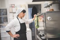 Женщина-пекарь смотрит на духовку на кухне — стоковое фото