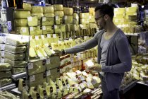 Joven seleccionando queso en el puesto de delicatessen, Sao Paulo, Brasil - foto de stock