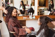 Chica y madre cogidas de la mano mientras tienen su pelo peinado en el salón de belleza - foto de stock