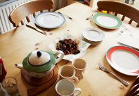 Teapot, mugs and plates set on wooden table — Stock Photo