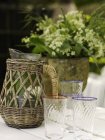 Vintage wicker jug and drinking glasses on garden table — Stock Photo