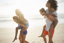 Young man and woman piggybacking friends in beach race, Cape Town, South Africa — Stock Photo